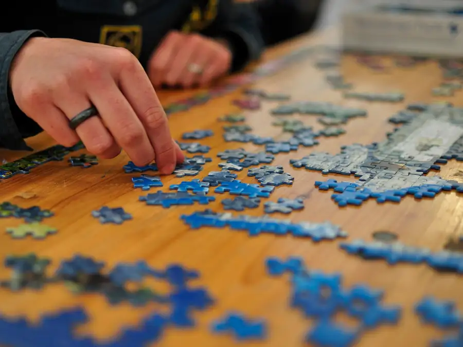 Hands fitting jigsaw pieces together on a wooden table