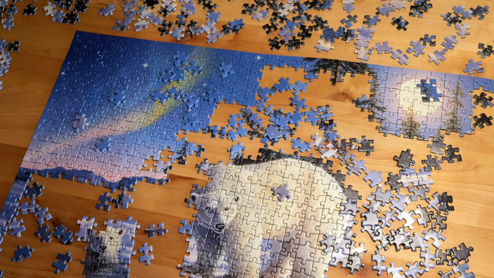 A half-finished jigsaw puzzle on a wooden table with loose pieces around it